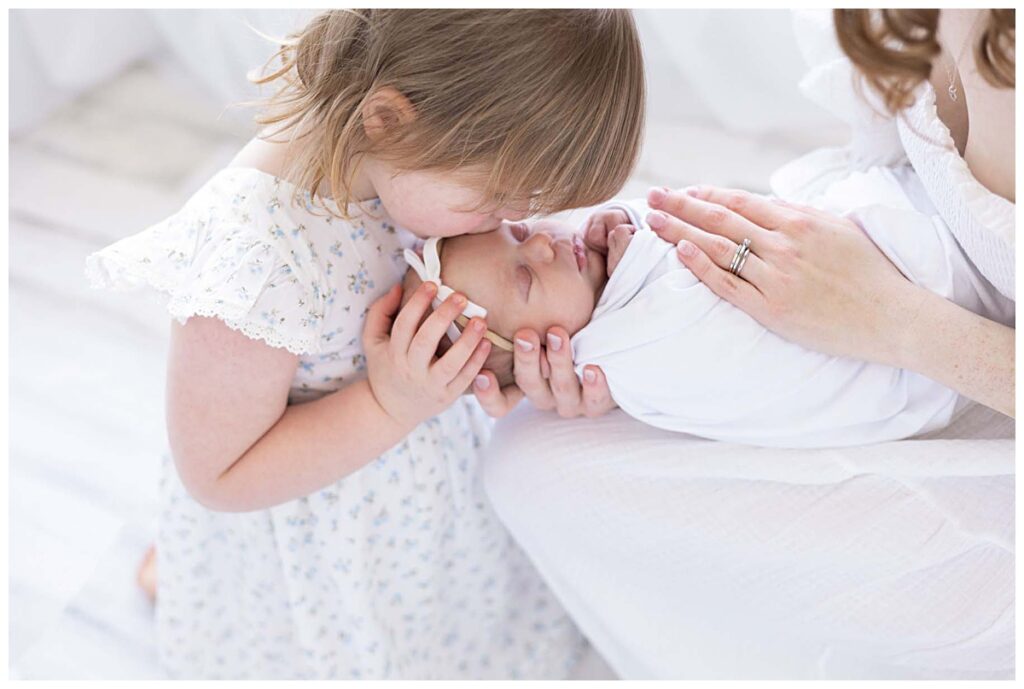 Toddler kissing newborn baby's head during session with Manchester NH Newborn Photographer Kathleen Jablonski.