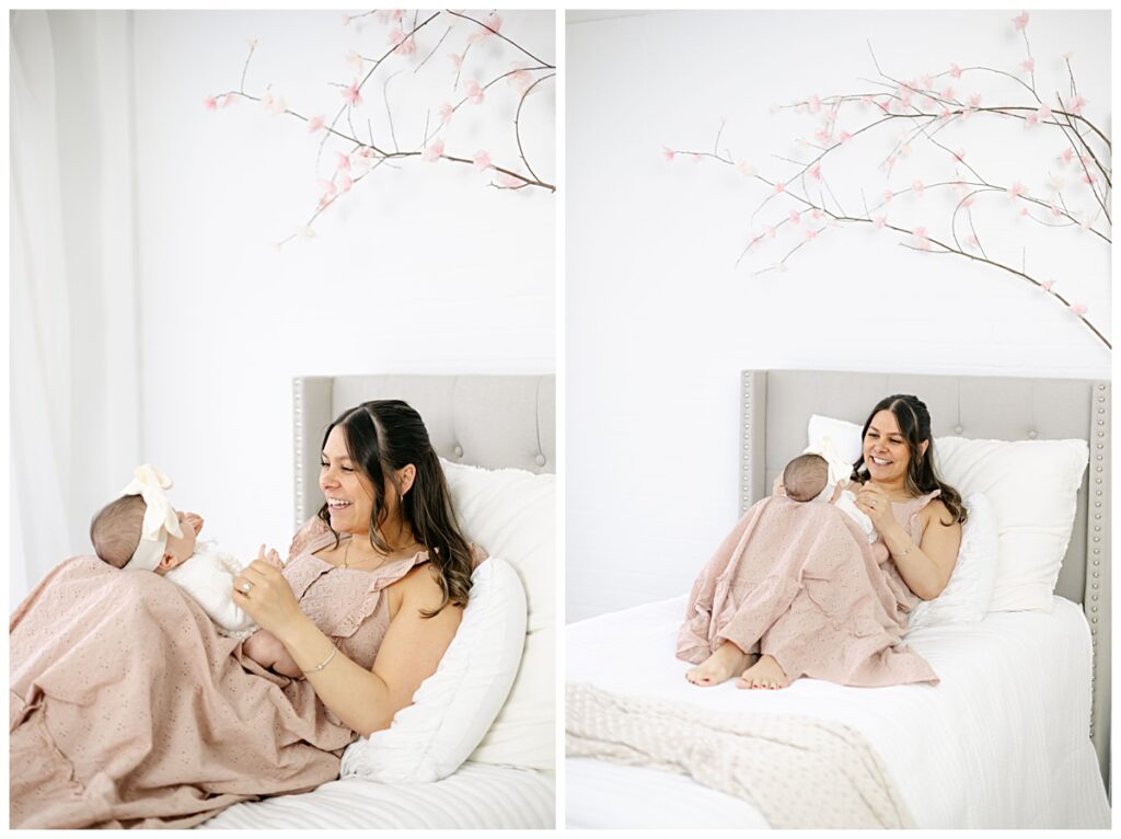 Mother and newborn baby playing on a bed in Kathleen Jablonski Photography white studio space in Manchester NH.