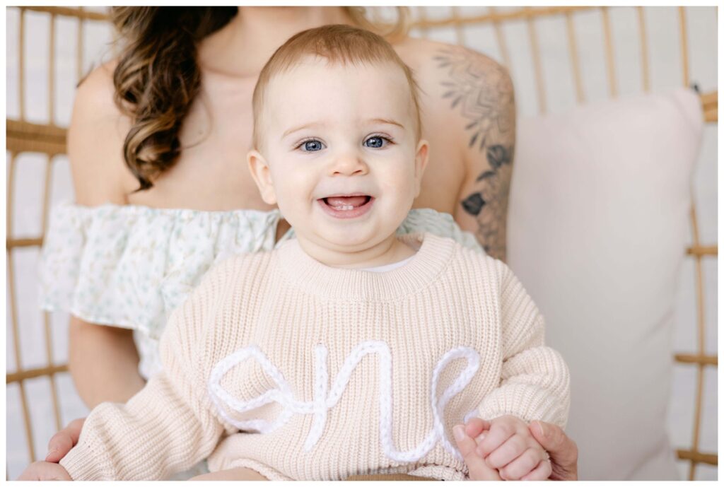 Little boy during Milestone session with Kathleen Jablonski Photography in studio wearing a ONE sweater sitting with mom.