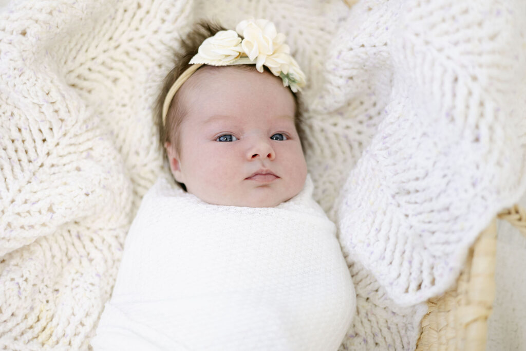 Newborn photo of a little girl with a bow and swaddled in a white swaddle. 